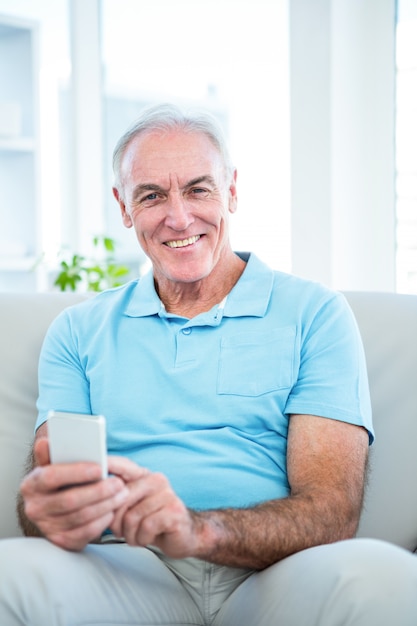Ritratto dell&#39;uomo senior senior che utilizza smartphone mentre sedendosi sul sofà a casa