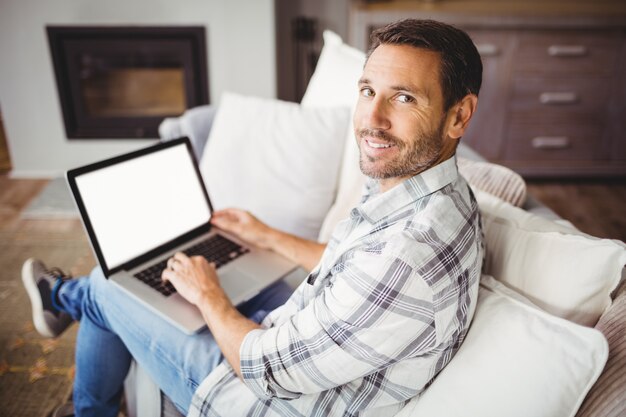 Ritratto dell'uomo sorridente che per mezzo del computer portatile