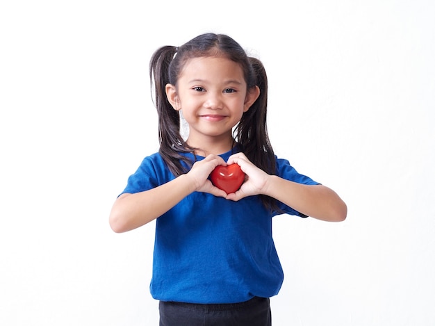 Ritratto della bambina che tiene cuore rosso sulla parete bianca. Spazio per il testo