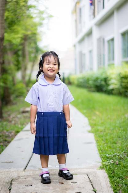 Ritratto della bambina felice in uniforme scolastica tailandese che sta nel parco