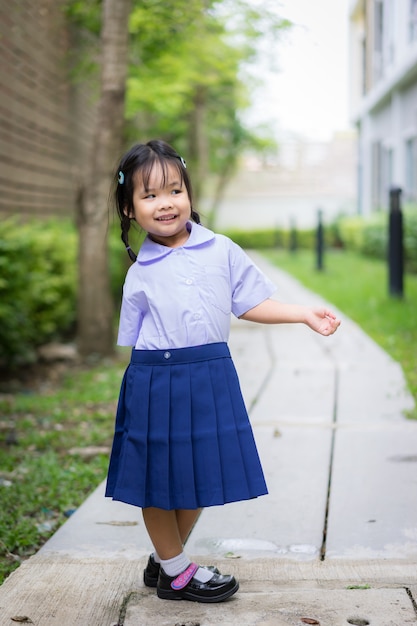 Ritratto della bambina felice in uniforme scolastica tailandese che sta nel parco