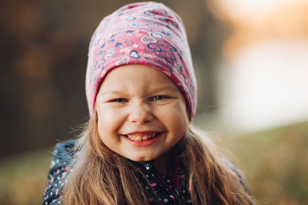 Ritratto della bambina graziosa felice in giacca e cappello trascorrere del tempo nel parco