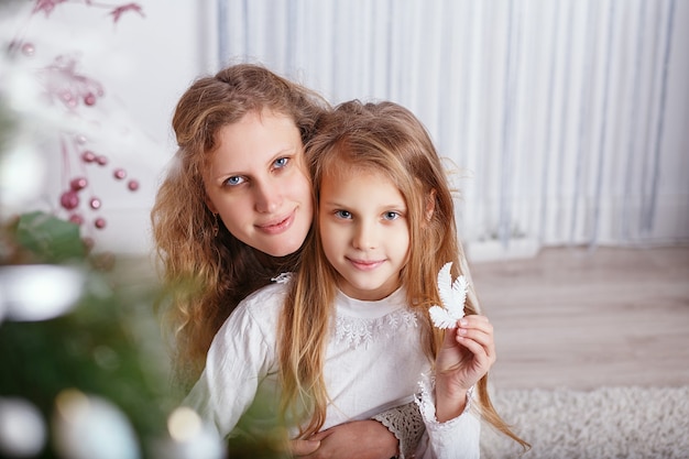 Ritratto della bambina sorridente felice con la madre che si siede vicino all'albero di Natale