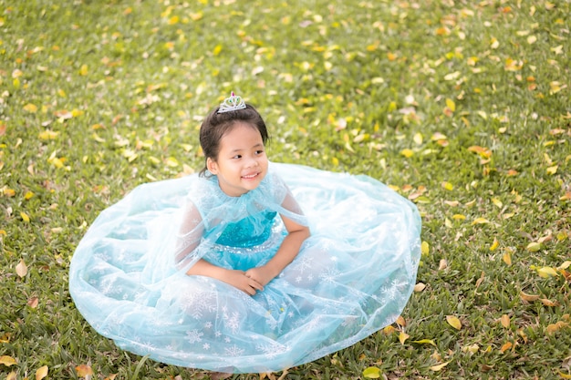 Ritratto della bambina sorridente in costume della principessa che si siede sull'erba nel parco