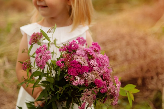 Ritratto della bambina sveglia che tenendosi per mano mazzo dei fiori rosa su un campo
