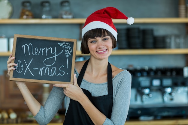 Ritratto della cameriera di bar che mostra ardesia con il segno allegro di natale