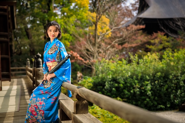 Ritratto della donna asiatica che porta kimono blu giapponese ed ombrello sulla mano della tenuta nel parco