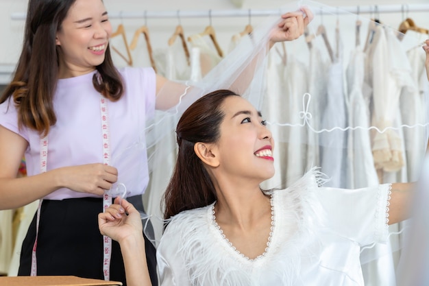 Ritratto della donna asiatica che sceglie vestito in un negozio con l'assistente del sarto.