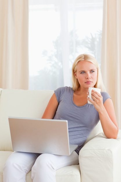 Ritratto della donna che mangia un tè mentre tenendo un computer portatile