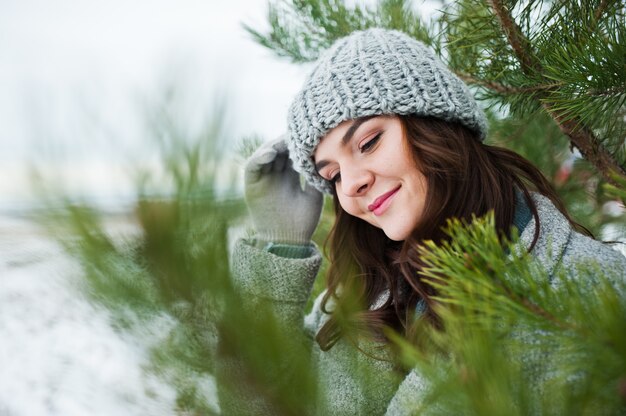 Ritratto della donna delicata in cappotto e cappello grigi contro l'albero di Natale all'aperto.