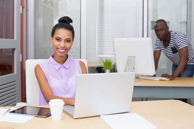 Ritratto della donna di affari che per mezzo del computer portatile