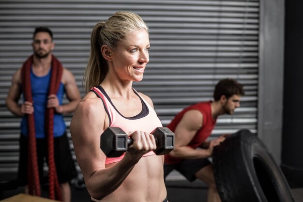 Ritratto della donna di misura che alza i dumbbells alla palestra del crossfit