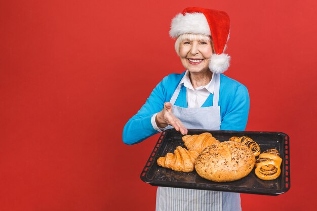 Ritratto della donna invecchiata allegra abbastanza affascinante con la grinza che mostra gesturing i prodotti da forno casalinghi dolci