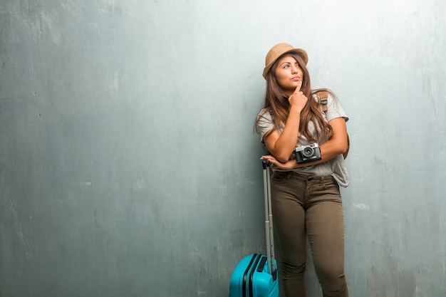 Ritratto della donna latina del giovane viaggiatore contro un muro che pensa e che osserva in su