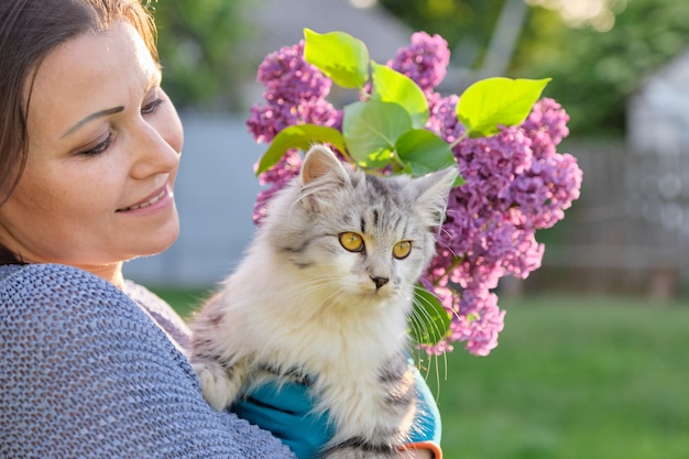 Ritratto della donna matura che tiene l'animale domestico lanuginoso grigio del gatto in sue braccia