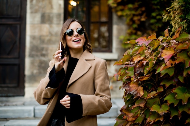 Ritratto della donna moderna che utilizza telefono cellulare all&#39;autunno all&#39;aperto