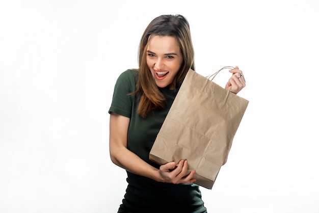 Ritratto della donna mora sorridente con il sacchetto della spesa in sue mani. Giovane ragazza felice che tiene il sacchetto della spesa di carta isolato