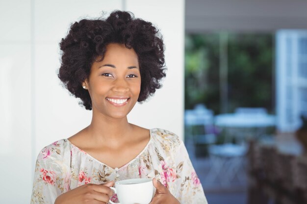 Ritratto della donna sorridente che tiene tazza bianca nella cucina