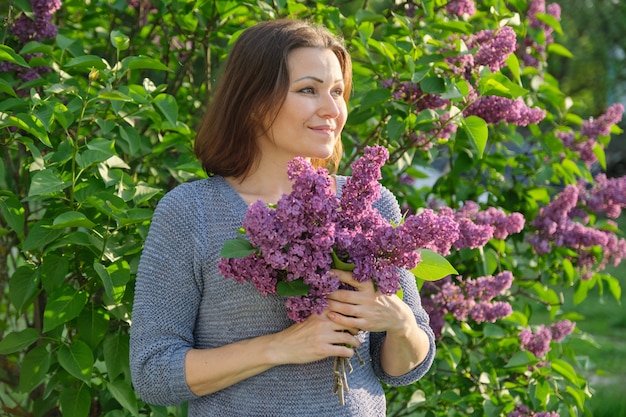 Ritratto della donna sorridente matura in giardino con il mazzo dei lillà