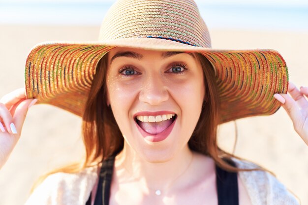 Ritratto della donna sorridente sul cappello di paglia da portare della spiaggia