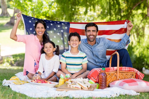 Ritratto della famiglia felice che tiene una bandiera americana nel parco