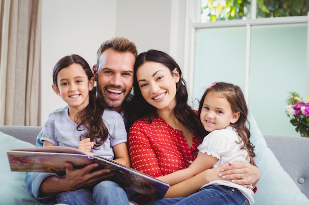 Ritratto della famiglia felice con il libro illustrato sul sofà