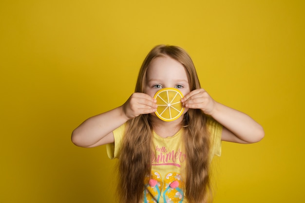 Ritratto della fetta sorridente della tenuta della bambina di occhio vicino del limone che esamina il primo piano di mezzo della macchina fotografica