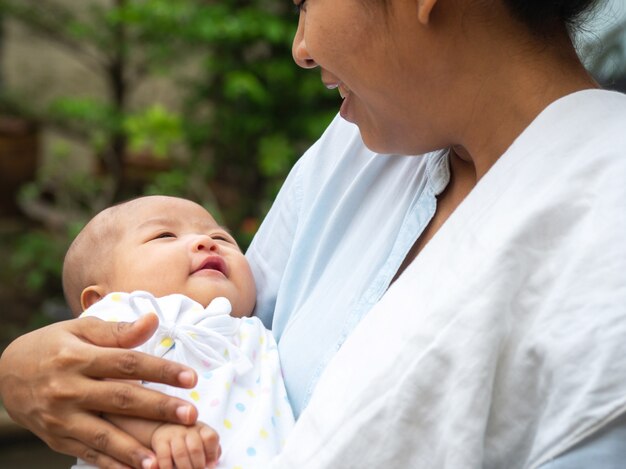 Ritratto della madre felice dell&#39;Asia che tiene il suo bambino dolce neonato vestito.