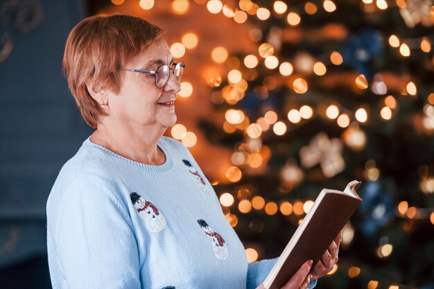 Ritratto della nonna che sta in piedi nella stanza decorata del nuovo anno con il libro.