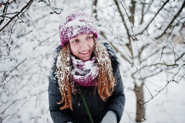 Ritratto della ragazza al giorno nevoso di inverno vicino agli alberi innevati.