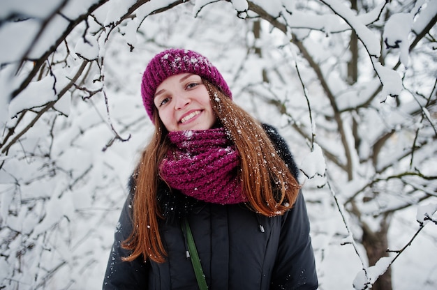 Ritratto della ragazza al giorno nevoso di inverno vicino agli alberi innevati.
