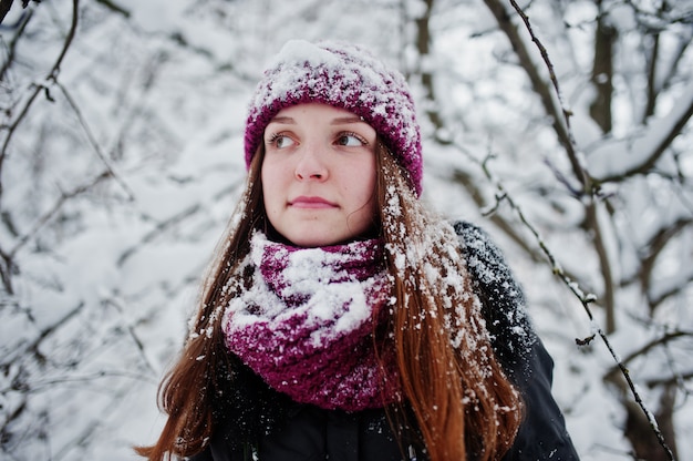 Ritratto della ragazza al giorno nevoso di inverno vicino agli alberi innevati.