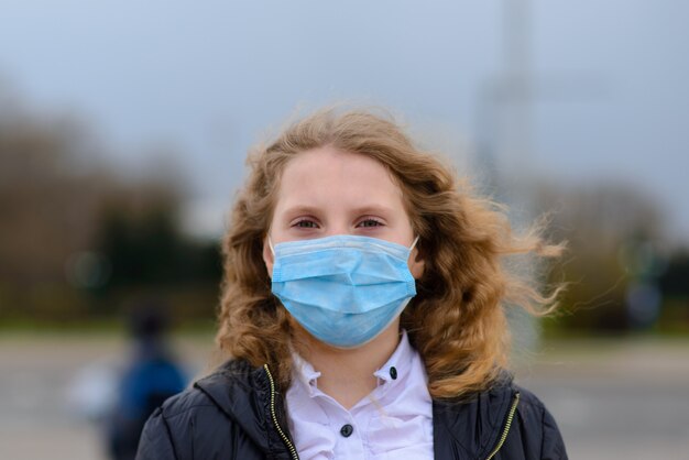 Ritratto della ragazza caucasica triste nella maschera di protezione alla città e nel parco all'aperto. Quarantena a distanza sociale del coronavirus.