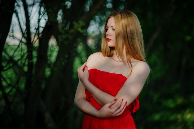 Ritratto della ragazza dei capelli chiari sul vestito rosso in giardino.