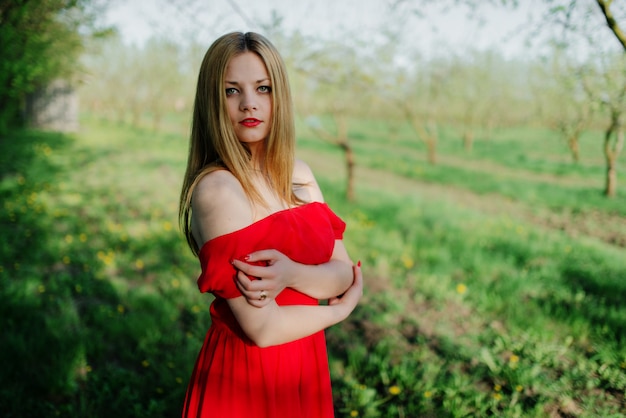 Ritratto della ragazza dei capelli chiari sul vestito rosso in giardino.