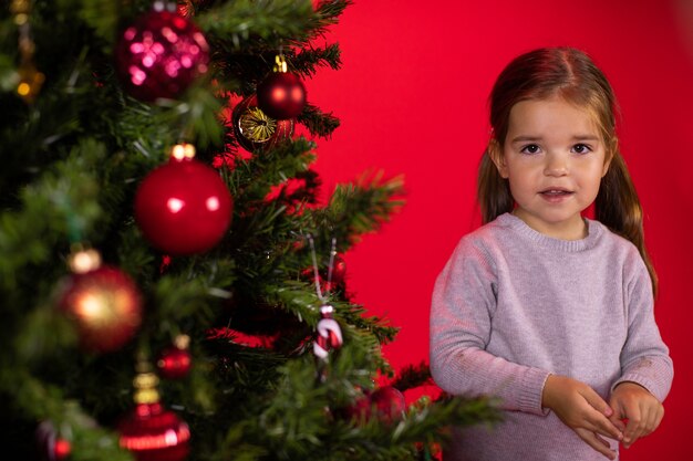 Ritratto della ragazza del bambino accanto all'albero di Natale