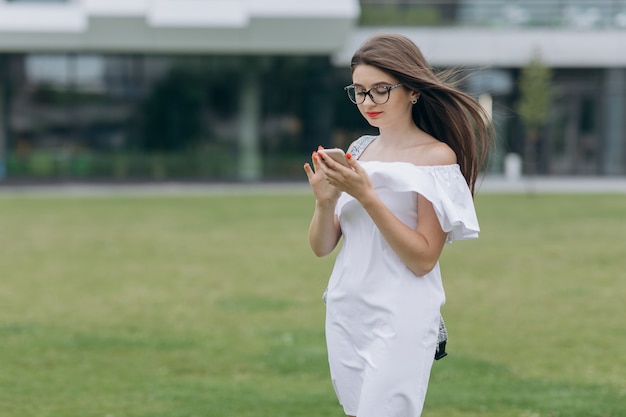 Ritratto della ragazza dell'adolescente dello studente con lo smartphone nell'università all'aperto