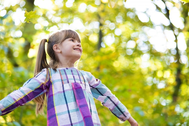 Ritratto della ragazza graziosa felice del bambino divertendosi nella foresta di autunno. Bambino femminile positivo che gode del giorno caldo nel parco dell'autunno.