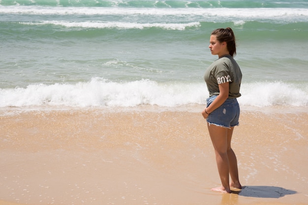 Ritratto della ragazza in cima verde e jeans del denim su una spiaggia