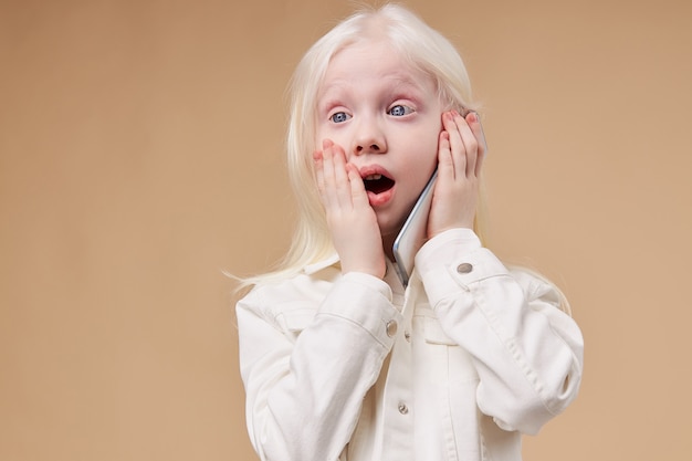 Ritratto della ragazza sorpresa del bambino albino con il telefono