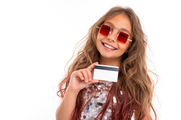 Ritratto della ragazza sorridente in occhiali da sole rossi quadrati che giudicano la carta assegni di plastica isolata