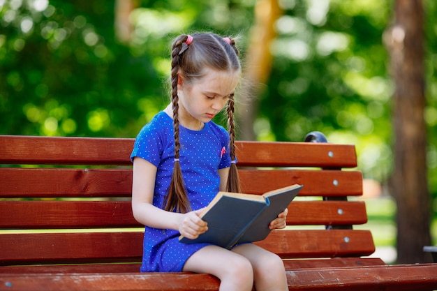 Ritratto della scolara su un libro di lettura del banco. Parco cittadino di sfondo.