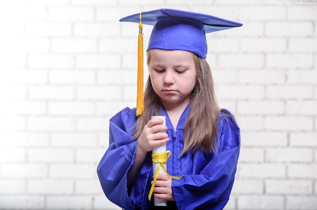 Ritratto della scolara sveglia con il cappello di graduazione in aula