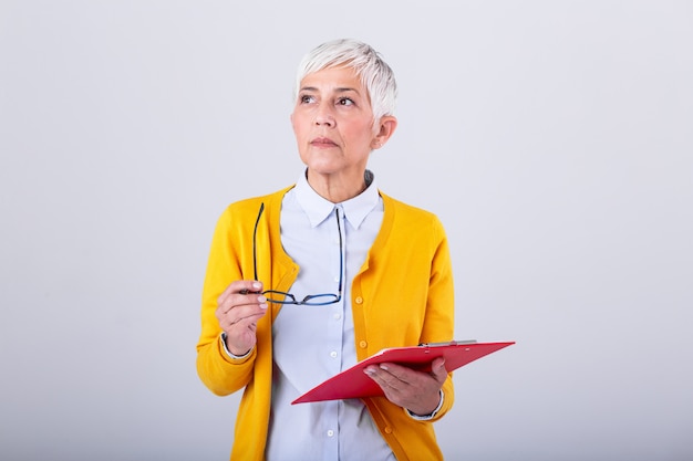 Ritratto delle donne di affari maturi con la lavagna per appunti e il documento a disposizione con lo spazio della copia isolato sulla parete bianca. Donna di affari creativa premurosa che distoglie lo sguardo nell'ufficio