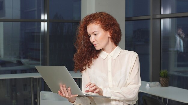 Ritratto delle free lance moderne della donna con il computer portatile in mani