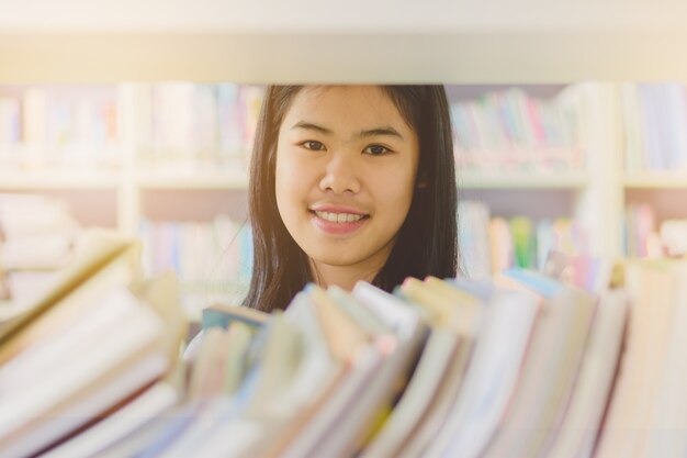 Ritratto dello studente asiatico intelligente che legge e che fa ricerca nella biblioteca di istituto universitario