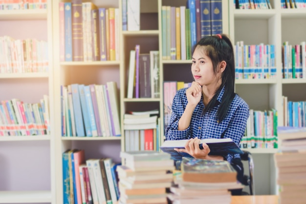 Ritratto dello studente asiatico intelligente che legge e che fa ricerca nella biblioteca di istituto universitario