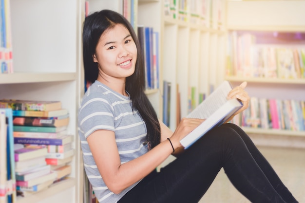 Ritratto dello studente asiatico intelligente che legge e che fa ricerca nella biblioteca di istituto universitario