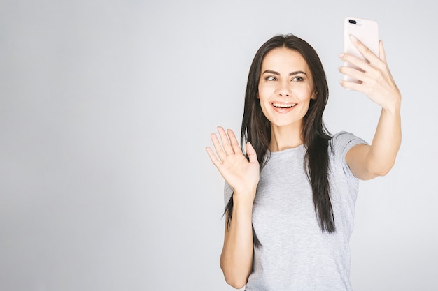 Ritratto dello studio di bella donna che sorride con i denti bianchi e che fa selfie, fotografandosi sopra fondo bianco.