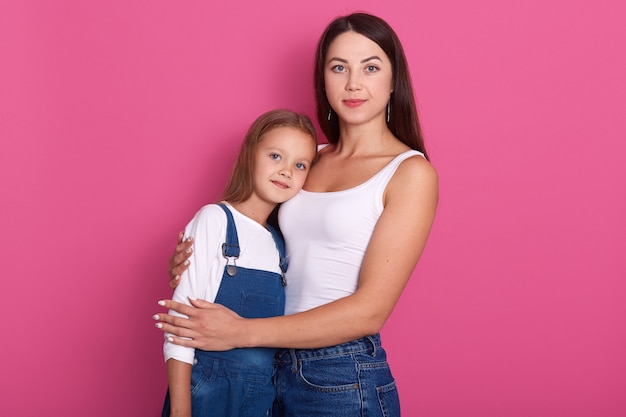 Ritratto dello studio di giovane madre attraente che abbraccia la sua piccola figlia